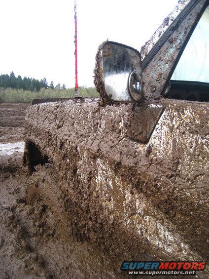 Mud-covered vehicle fender and side mirror stuck in mud, with a red antenna visible