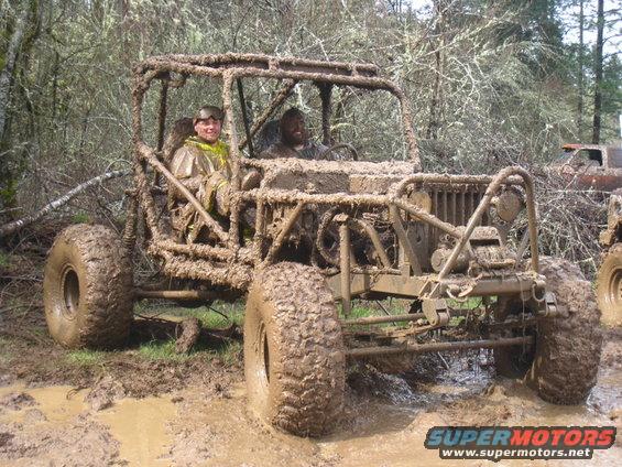 Mud-covered off-road buggy with two people in a wooded area