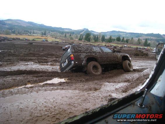 Mud-covered SUV stuck in a muddy field with other vehicles in the background