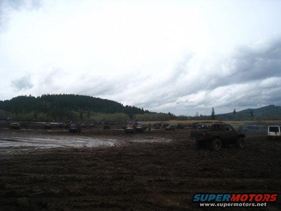 Muddy field with many off-road vehicles under a cloudy sky