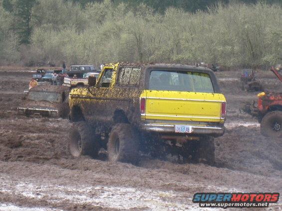 Yellow SUV with lifted suspension driving through mud, rear view