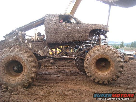 Mud-covered monster truck side view with large tires and exposed engine components