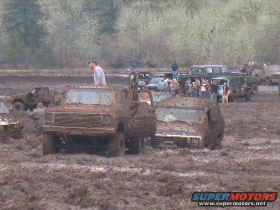 muddy trucks stuck in a field with people around