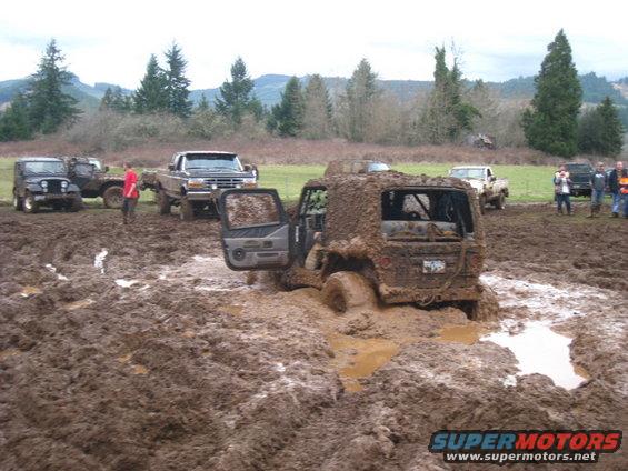 Mud-covered Jeep Wrangler stuck in mud, rear view, doors open