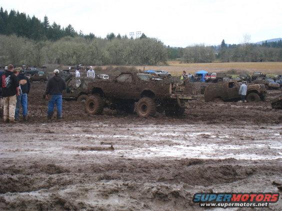 Muddy off-road vehicles and people gathered in a muddy field
