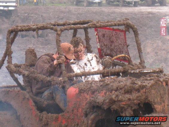 Mud-covered buggy with two guys inside, steering wheel visible