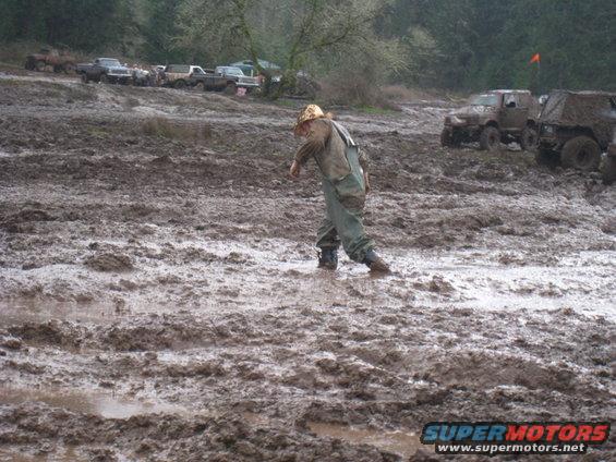 Person walking through mud with several off-road vehicles in the background