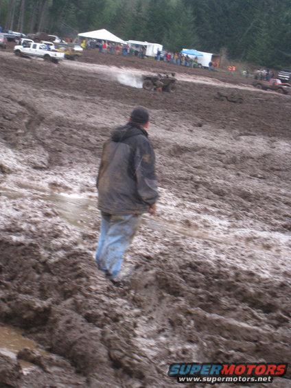 Person watching ATVs in a mud pit with tents and spectators in background