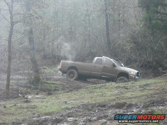 Brown pickup truck stuck in mud with steam coming from exhaust