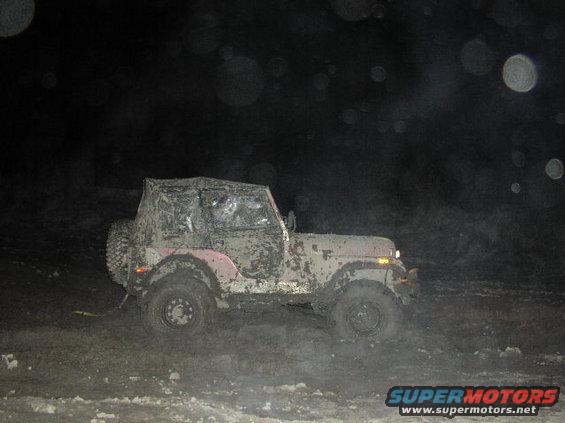 Mud-covered Jeep CJ-7 driving through mud at night