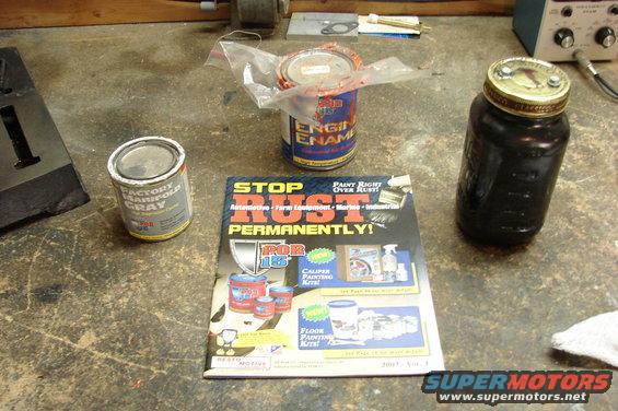 Two cans of paint and a jar of dark liquid on a workbench next to a magazine about rust prevention