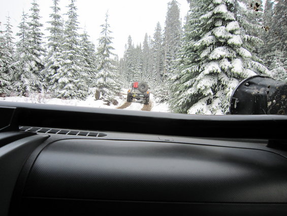 2007 Jeep Wrangler driving on a snow-covered dirt road in a forest, seen from inside another vehicle