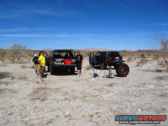 1986 Ford Bronco lifted with jack, another Bronco with open trunk nearby
