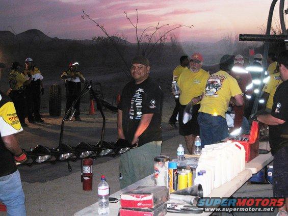 People gathered around equipment and supplies at dusk, with a large light bar in the foreground