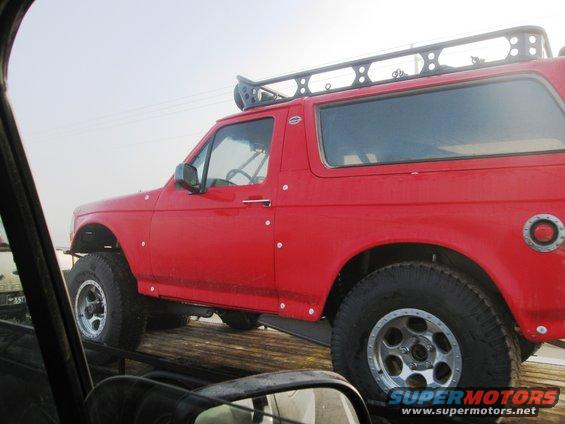 Red SUV with a roof rack, lifted suspension, and aftermarket wheels, seen from the side