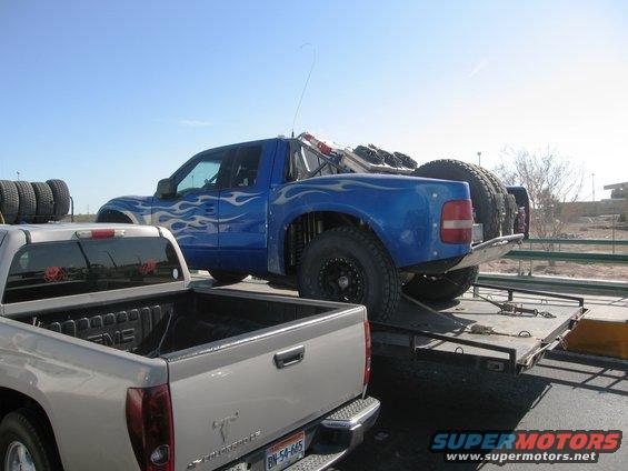 Blue off-road truck with flame decals on a trailer, spare tires visible
