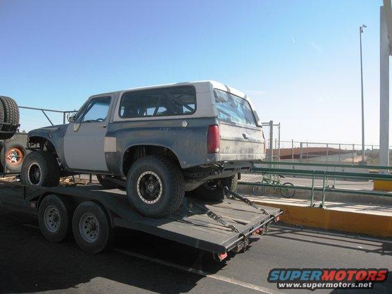 1986 Ford Bronco on a flatbed trailer, modified with large tires and fender flares