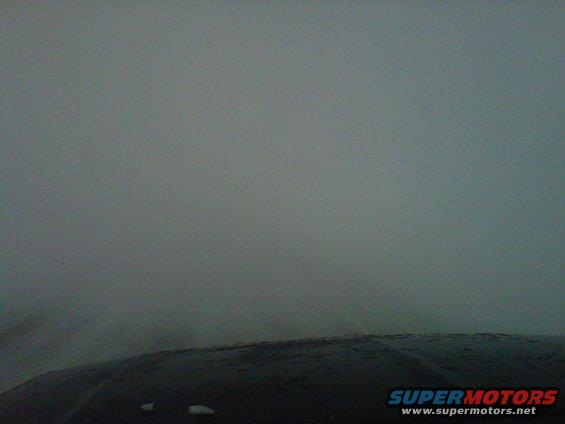 Dark hood of a vehicle with a few white spots, seen from a low angle against a hazy sky