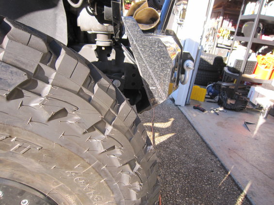 Close-up of a large off-road tire with aggressive tread, showing part of a metal bumper with a tow hook