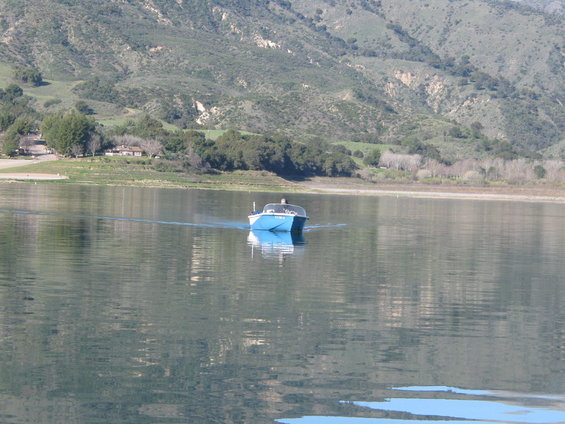 Blue boat moving across a lake with hills in the background