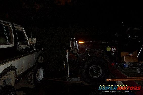 Two SUVs parked at night, one is white and brown, the other is dark colored with stickers