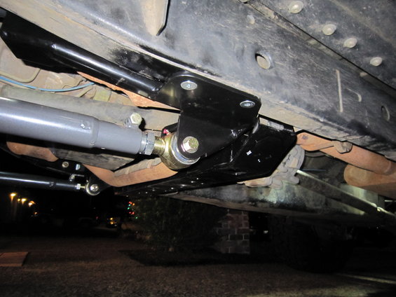 Underside of vehicle showing black aftermarket suspension arms and brackets attached to the frame