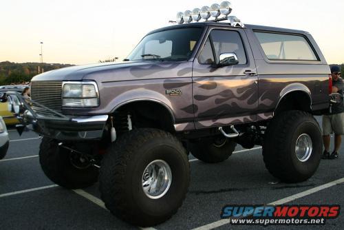 1995 Ford Bronco with custom flame decals and large off-road tires, parked in a lot