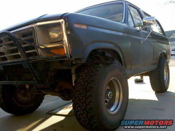 Dark blue Ford Bronco with off-road tires and a brush guard, viewed from a low front 3/4 angle