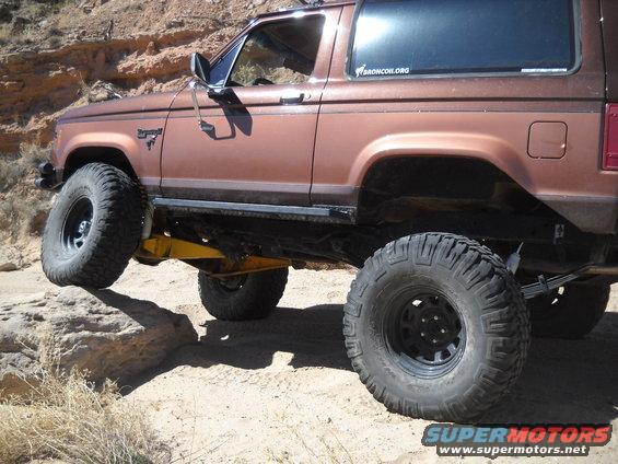 1986 Ford Bronco II with large tires on rocky terrain. Bronco.org sticker on rear window