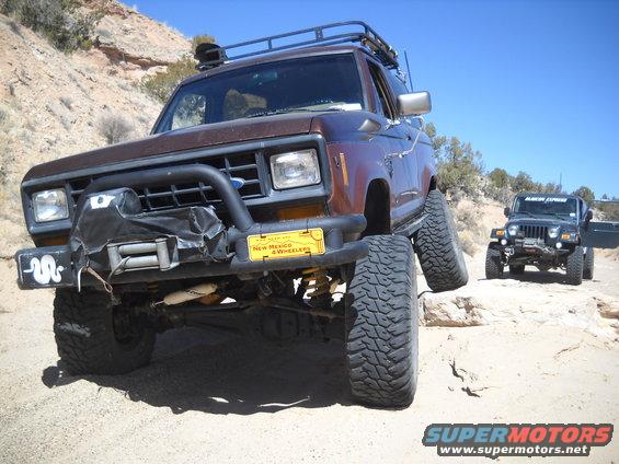 Brown 1986 Ford Bronco II with winch and roof rack on rocky terrain, another Jeep in background