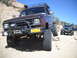 1986 Ford Bronco II - Two off-road vehicles navigate a rocky trail under a clear blue sky.