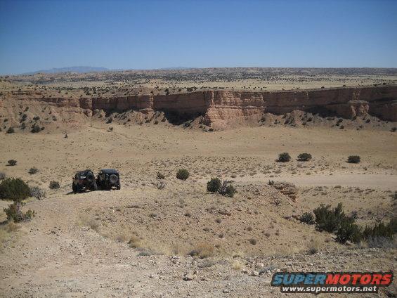 Two dark SUVs parked in a desert landscape with a canyon in the background