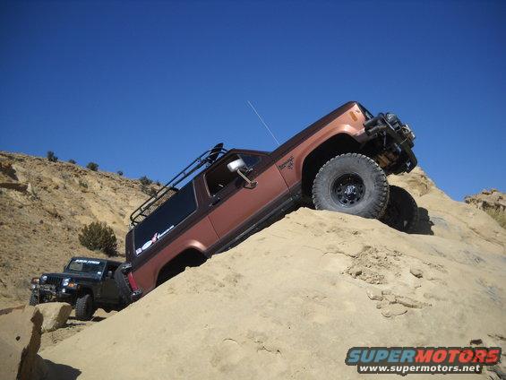 Brown 1986 Ford Bronco II climbing a sandy hill with a black Jeep behind it