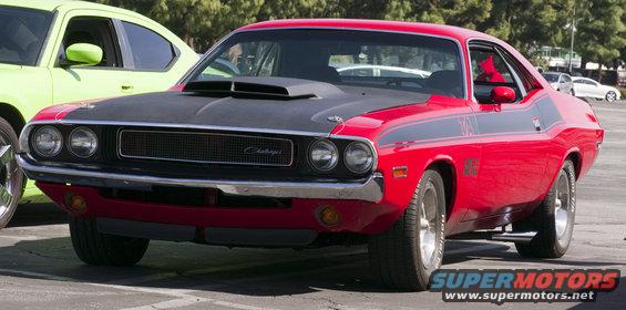 Red 1970 Dodge Challenger with black hood scoop and racing stripes parked next to a green car
