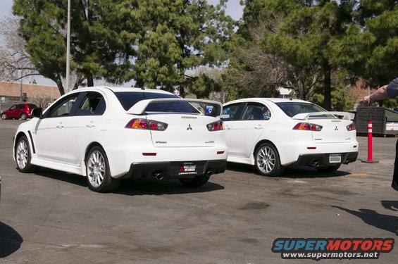 Two white Mitsubishi Lancer Evolutions parked side-by-side, rear view. One has a license plate frame that says 'Evolution'