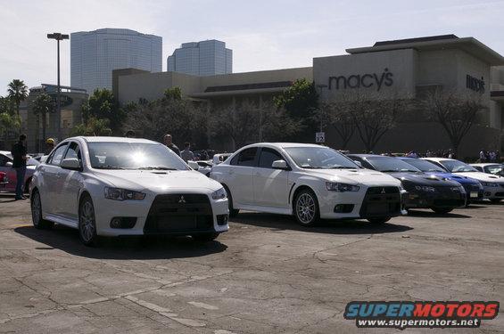 Two white Mitsubishi Lancer Evolution cars parked in a lot with Macy's department store in the background