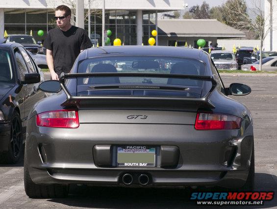 Rear view of a gray Porsche 911 GT3 with a spoiler and dual exhaust. A man stands beside it