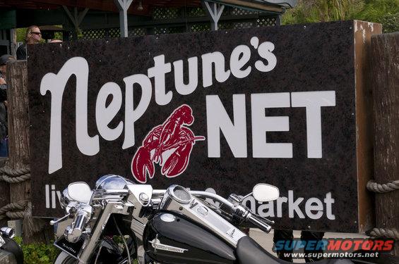 Chrome motorcycle handlebars and tank in front of Neptune's Net sign