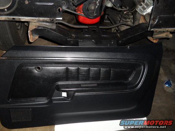 Black vinyl car door panel with chrome trim and a red engine component visible above
