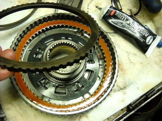 Close-up of an automatic transmission clutch pack with a hand holding a friction ring. Tube of assembly lube nearby
