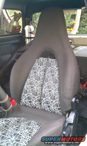 Interior shot of a car seat with a unique white geometric pattern on the backrest and seat cushion. A silver tank is visible behind the seat