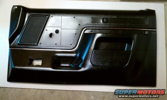 Black car door panel with speaker grille, chrome trim, and armrest