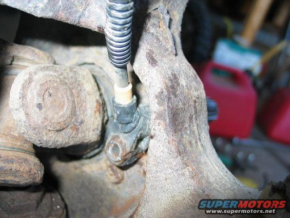 Close-up of rusty suspension part with ABS sensor and wiring. Red gas cans in background