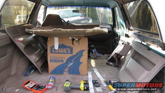 Interior of a vehicle with parts removed, tools, and a Lowe's box. Another vehicle is visible through the windshield