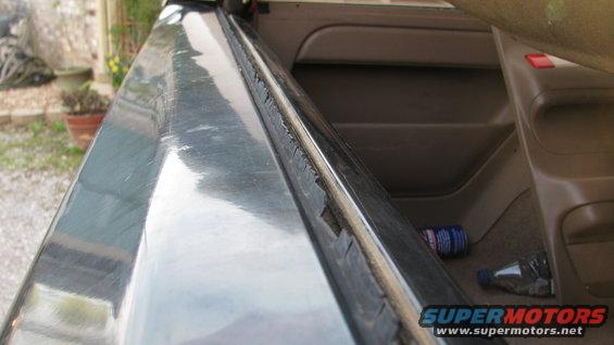 Interior door frame and dashboard of a vehicle with a worn rubber seal. A can and bottle are visible on the floor