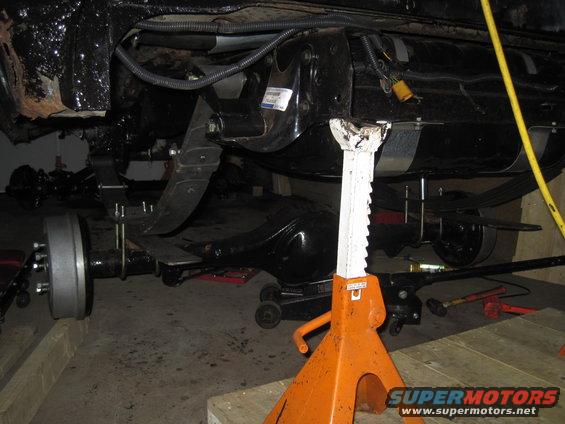 Undercarriage of a vehicle on jack stands, showing suspension and rear axle components
