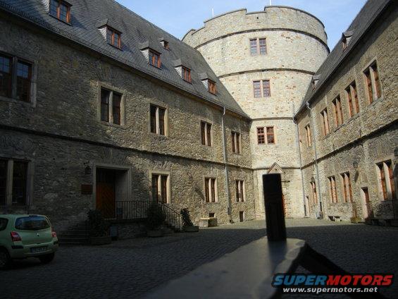 Small green hatchback parked in a stone courtyard of a castle