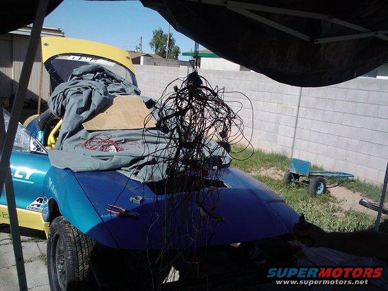 Blue car with yellow hood, covered with tarp and tangled wires. Tools on the trunk