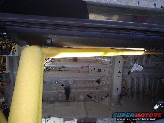Interior view of a car's stripped-down floor and roll cage with yellow padding
