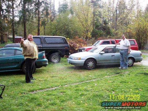Black Ford Bronco with a camper shell, parked next to a green Mustang and a light blue sedan
